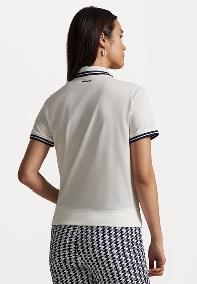 Biely polokošeľa s námorníckymi pruhmi na golieri a rukávoch; má priliehavý strih a logo na chrbte. Nosené s vzorovanými námorníckymi nohavicami.