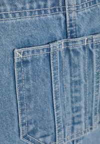 Ljusblå denimtyg med en synlig bakficka. Sömmen är i kontrasterande vitt och texturen är något sliten med en slät finish.