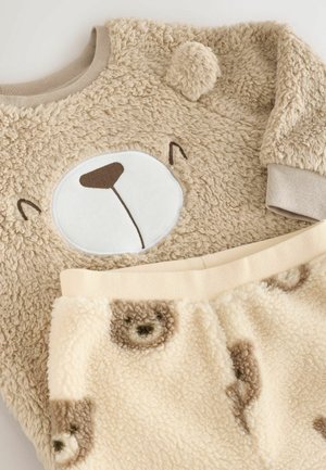 Beige fleece trøje med bjørneansigt design og blød tekstur, parret med cremefarvede bukser med bjørneprint. Rundet krave og elastisk talje.