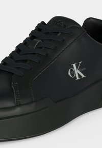 Μαύρο low-top sneaker Calvin Klein με παχύ πάτο, στρογγυλεμένη μύτη, μαύρα κορδόνια και λευκό λογότυπο "cK Calvin Klein" στο πλάι.