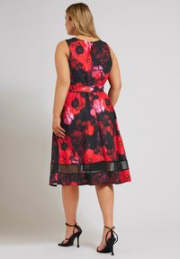 Vestido floral con un corsé ajustado, colores rojo y negro, detalles de malla transparente en el dobladillo y un cinturón de tela en la cintura.