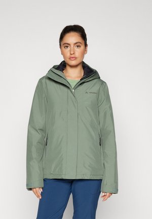 Veste imperméable verte avec capuche, présentant des poches latérales zippées et un intérieur noir contrastant. Texture lisse et coupe décontractée.