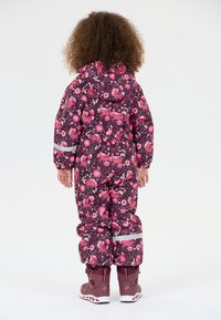 Lyserød og lilla blomstermønstret vinterdragt med hætte, reflekterende striber og elastiske manchetter. Båret med matchende bordeaux støvler.