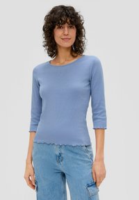  Lichtblauwe geribde top met 3/4 mouwen, ronde halslijn en scalloped zoom; gedragen met losse lichtgekleurde denim cargo broeken.