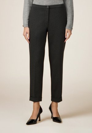 Pantalon gris sur mesure avec ourlets retroussés porté avec des chaussures à talons noirs et un haut gris à manches longues, montré du milieu du torse jusqu'aux pieds.