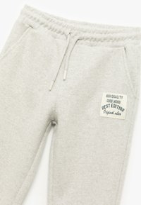 Lys grå sweatpants lavet af struktureret stof, med justerbar talje, sidelommer og et vævet label med tekst accenter.