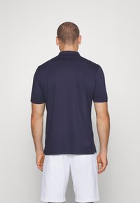 Navy polo shirt with a collar, short sleeves, and a straight hem, paired with white shorts. Smooth, lightweight fabric with no visible logos.