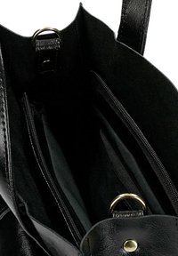 Wnętrze torby tote z czarnej skóry z wieloma zamykanymi kieszeniami, gładką fakturą oraz złotym metalowym pierścieniem na górze do zamykania.