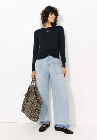 Pull noir côtelé, jean large taille haute bleu clair, ballerines noires à clous et un sac fourre-tout en cuir léopard brun avec des poignées doubles.