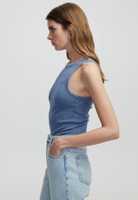 Niebieski prążkowany top na ramiączkach z wysokim dekoltem i szerokimi otworami na ramiona, połączony z jasnoniebieskimi spodniami dżinsowymi z wysokim stanem. Gładka faktura, dopasowany krój.