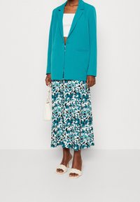 Tyrkysový blejzr se dvěma předními kapsami, kombinuje se s dlouhou sukní s květinovým potiskem v tyrkysové a bílé barvě. Béžové propletené nazouváky, bílá kabelka.