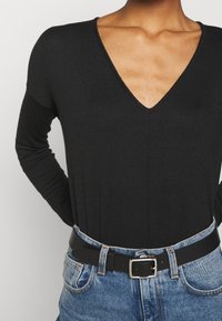Haut noir à manches longues en V associé à un jean en denim bleu taille haute et une ceinture noire avec une boucle rectangulaire en argent.