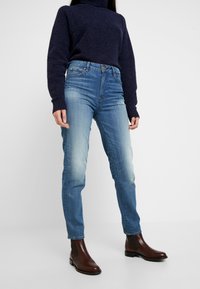 Blå denimjeans med en blekt tvätt, rak bendesign, femfickorsstil och knäppning med knapp. Bärs tillsammans med en mörk stickad tröja och bruna stövlar.