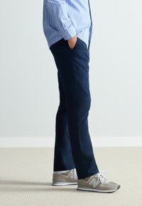 Pantaloni bleumarin din țesătură, cu croială slim, având buzunare laterale. Asortați cu adidași gri deschis, cu accente albe.
