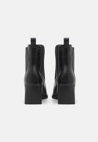 Bottes de cheville en cuir noir avec un talon épais, des panneaux latéraux élastiques et une texture lisse, dotées de deux tirants à l'arrière.