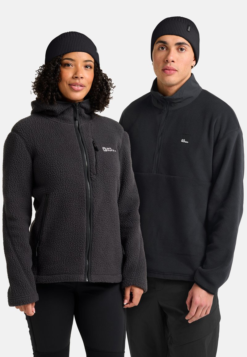Due persone che indossano giacche in pile nere e berretti di lana neri abbinati, in piedi fianco a fianco su uno sfondo bianco.