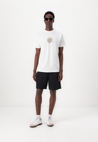 White cotton t-shirt with a colorful graphic on the front, paired with knee-length black shorts and white sneakers with gray accents.