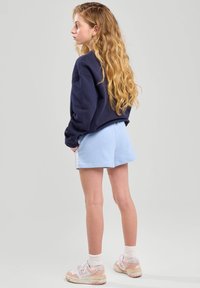Felpa navy, pantaloni corti azzurri con tasche e sneakers chiare con accenti pastel. Capelli acconciati in lunghe onde.