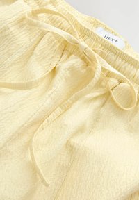 Helle gelbe Hose aus strukturiertem Stoff, mit einem elastischen Bund und einer gebundenen Kordel. Minimalistisches Design ohne Muster.