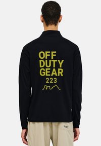 Schwarzes Langarmhemd aus strukturiertem Stoff mit großem gelbem Drucktext: "OFF DUTY GEAR 223" und einer geometrischen Skyline-Kontur auf der Rückseite.