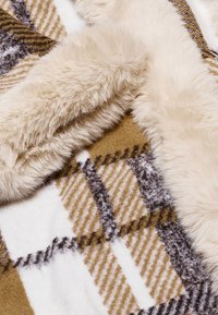 Texturiertes Überwurfdecke mit einem Karomuster in verschiedenen Brauntönen, Beige und Weiß, mit einem weichen, flauschigen cremefarbenen Rand.