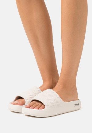 Sandales blanches à semelle plate avec des brides texturées et un design à bout ouvert. La semelle est plate avec un accent logo subtil sur le côté.