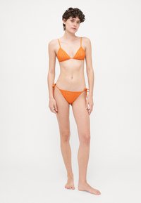 Oranž bikini komplekt, millel on sooniline tekstuur, kolmnurkne rinnahoidja õhukeste rihmadega ja reguleeritavad külje sidumised. Sile kangas, minimaalne disain.