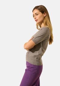 Pull gris à manches courtes en maille douce, associé à un pantalon violet avec une coupe droite et des poches arrière.