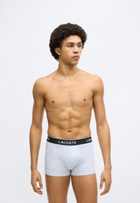 Boxer aderenti azzurri con fascia in vita nera con logo "LACOSTE", tessuto morbido, vestibilità aderente, con taglio classico e texture liscia.