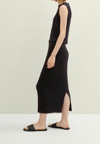 Černý texturovaný dvoudílný outfit, který obsahuje top s krátkým rukávem a dlouhou sukni s bočním rozparkem, doplněný černými nazouvacími sandály.