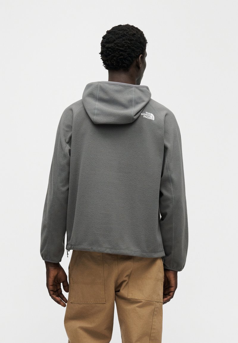 Gray fleece hoodie with a hood, featuring a logo on the back shoulder. Designed with a relaxed fit and zippered side pockets.