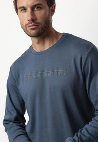 Camisa de manga larga azul marino de tejido suave, con cuello redondo y un logotipo impreso "ANTONIO MIRO 1979" en el pecho.