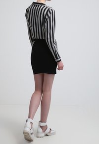 Mini gonna nera abbinata a una maglietta a righe bianche e nere con maniche lunghe. La modella indossa sandali bianchi con tacco spesso e cinturini alla caviglia.