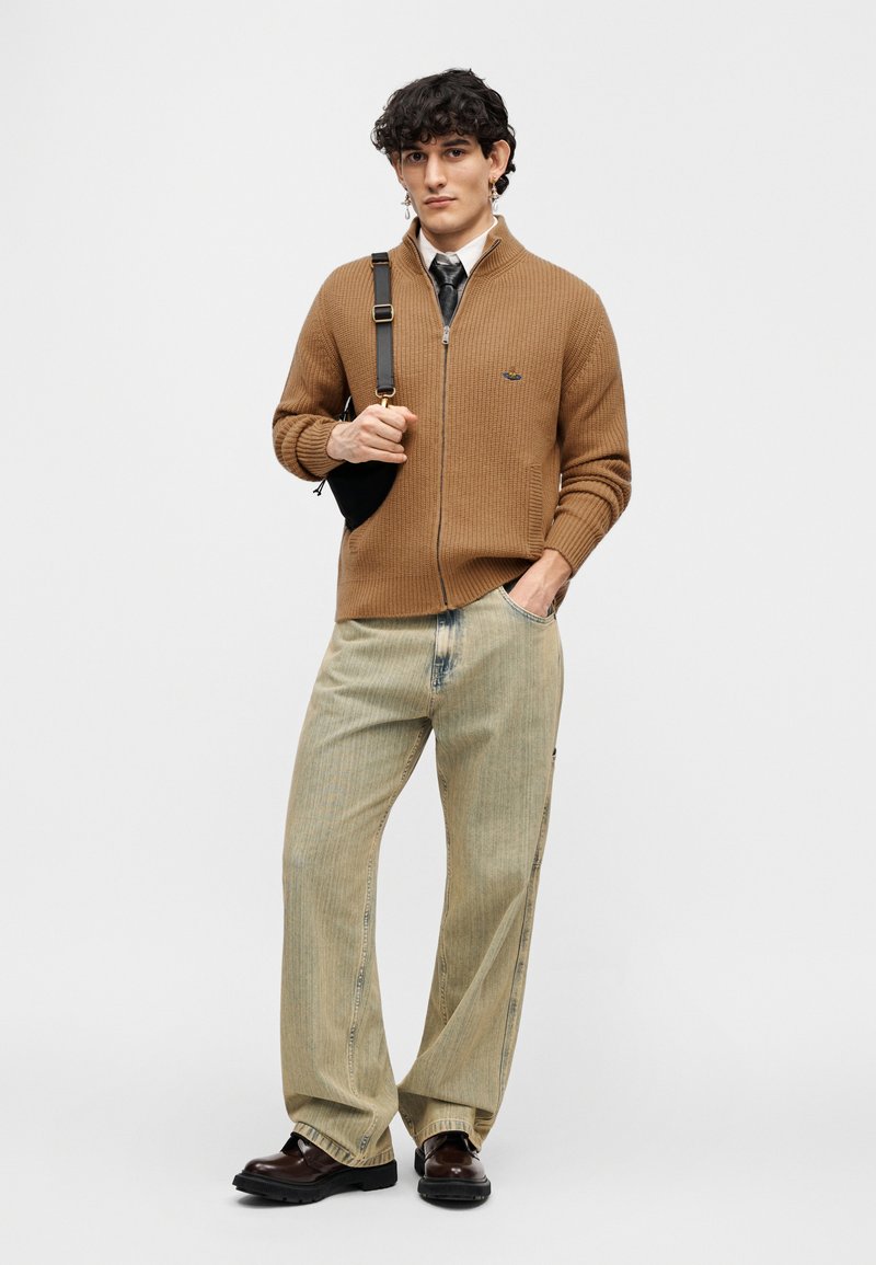 Brown ribbed zip-up sweater with high collar, light blue wide-leg jeans, and dark brown shoes. Includes a small black crossbody bag.