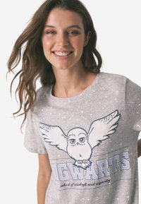 Grå bomulds t-shirt med et grafik af en ugle med vinger og "HOGWARTS" tekst nedenunder, prydet med stjernesymbolet og en afslappet pasform.