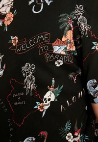 Zwarte stof met een kleurrijke print met Hawaiiaanse thema's, waaronder bloemen, een hula danseres en tekst die "WELKOM IN HET PARADIJS" zegt.