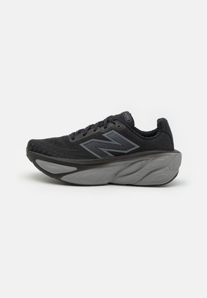 Chaussure de course New Balance noire et grise avec une semelle épaisse amortie et un design à lacets, vue de profil sur fond blanc.