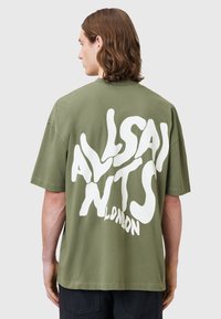Olive zielona bawełniana koszulka z oversize'owym krojem, z dużym białym napisem "ALLSAINTS LONDON" nadrukowanym na plecach. Krótkie rękawy.