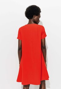 Robe rouge à manches courtes, en tissu lisse, avec un design légèrement évasé, un col rond modéré et une longueur arrivant au genou.