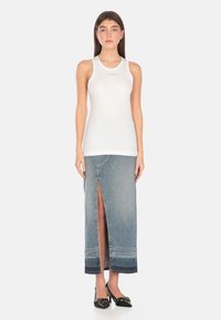 Top senza maniche bianco con logo, abbinato a una lunga gonna in denim azzurro chiaro con uno spacco frontale e cuciture in contrasto.