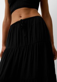 Schwarzer gestufter Rock aus leichtem Stoff mit einem Kordelzugbund. Verfügt über eine weiche Textur und ein fließendes Design.