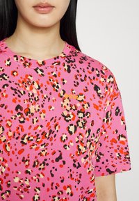 Lyserød t-shirt med korte ærmer, der har et leopardmønster i rød, sort og beige, med et lille "BOSS"-logo placeret på forsiden.
