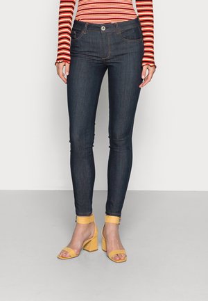 Jean slim bleu foncé porté avec un haut à manches longues rayé rouge et orange et des sandales à talons carrés jaunes.