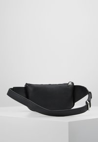 Borsa a tracolla nera in pelle con finitura testurizzata, chiusura con zip e tracolla regolabile con fibbia in metallo. Forma rettangolare.