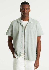 Chemise à manches courtes boutonnée en vert clair avec des rayures blanches, dotée d'un col, d'une coupe décontractée et d'un logo subtil sur la poitrine.