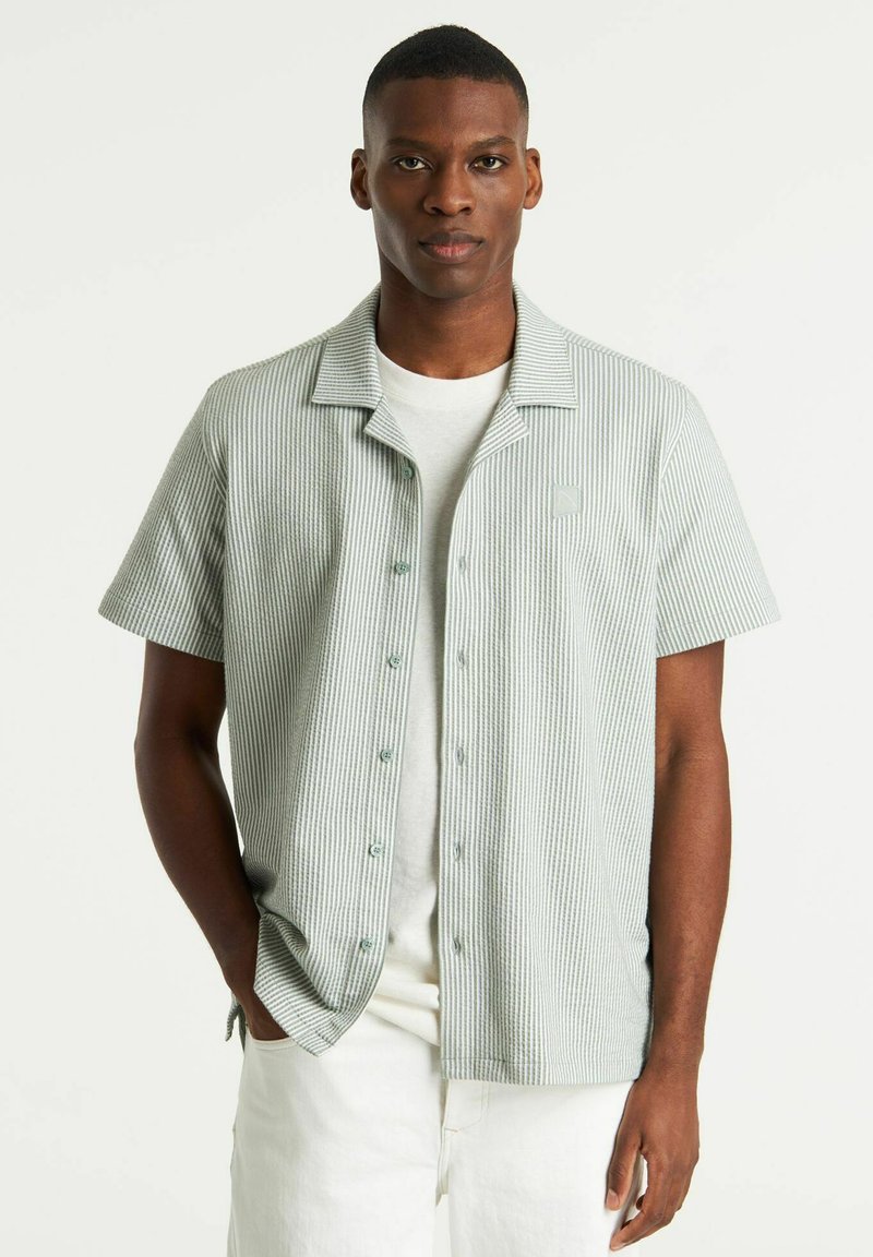 Chemise à manches courtes boutonnée en vert clair avec des rayures blanches, dotée d'un col, d'une coupe décontractée et d'un logo subtil sur la poitrine.
