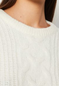 Weißer gestrickter Pullover mit einem gerippten Textur und einem Zopfmuster an der Vorderseite. Verfügt über einen weiten, weichen Halsausschnitt.