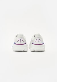 Baskets blanches avec un dessus texturé, des accents violets et bleus au niveau du talon, et une semelle rembourrée pour le soutien et le confort.