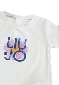 La maglietta bianca a maniche corte presenta una grafica colorata con lettere blu e un design di fiore rosa. Tessuto morbido con scollatura rotonda.