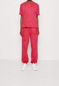 Rosa tie-dye t-shirt og matchende joggers, begge lavet af blødt stof. T-shirten har en rund halsudskæring; joggersne har en elastisk talje og ankelmanchetter.